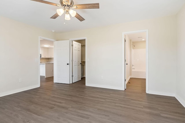 unfurnished bedroom featuring a walk in closet, wood finished floors, baseboards, and ensuite bathroom