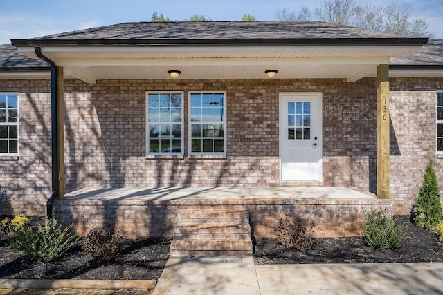 doorway to property with covered porch, brick siding, and a shingled roof