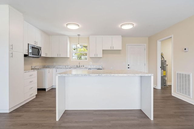 kitchen with visible vents, white cabinets, electric water heater, stainless steel microwave, and a center island