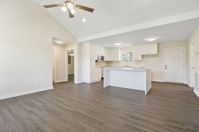 kitchen with stainless steel microwave, a kitchen island, baseboards, white cabinets, and a ceiling fan