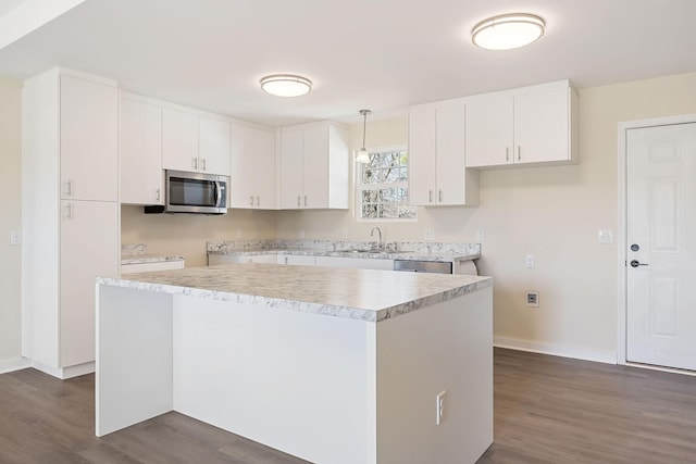kitchen featuring a sink, dark wood finished floors, stainless steel appliances, white cabinets, and hanging light fixtures