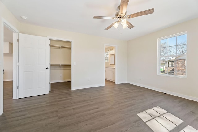 unfurnished bedroom featuring wood finished floors, baseboards, a ceiling fan, a closet, and a walk in closet