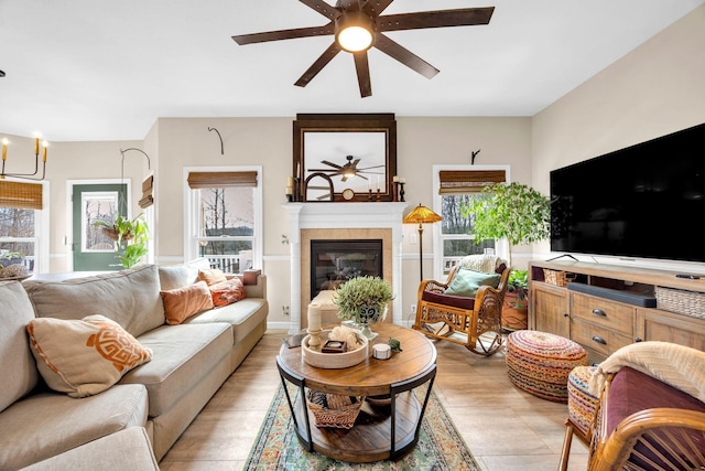 living area with ceiling fan with notable chandelier, a tiled fireplace, and a healthy amount of sunlight