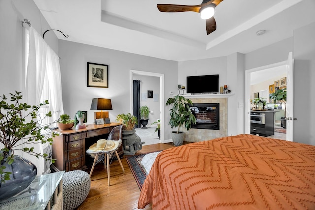 bedroom featuring a tray ceiling, a tile fireplace, and wood finished floors