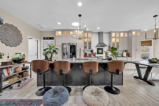 kitchen featuring a chandelier, a sink, wall chimney range hood, a large island, and stainless steel refrigerator with ice dispenser