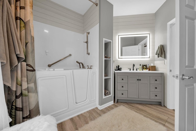 full bath with wooden walls, a bathtub, wood finished floors, and vanity