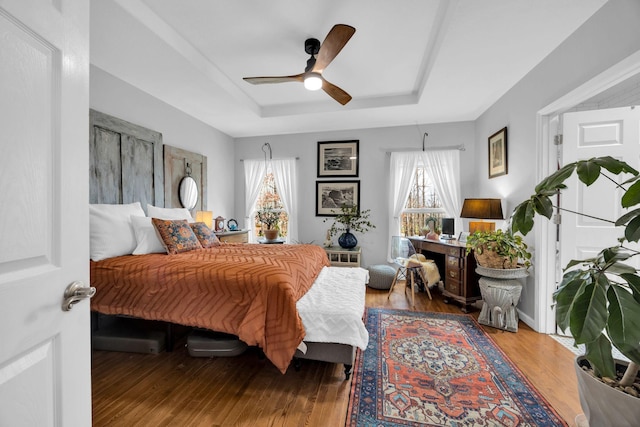 bedroom with ceiling fan, a tray ceiling, and wood finished floors