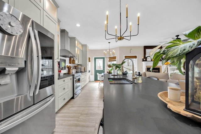 kitchen featuring wall chimney exhaust hood, appliances with stainless steel finishes, an inviting chandelier, a fireplace, and a sink