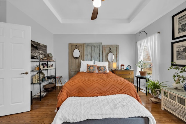 bedroom featuring a ceiling fan, a raised ceiling, baseboards, and wood finished floors