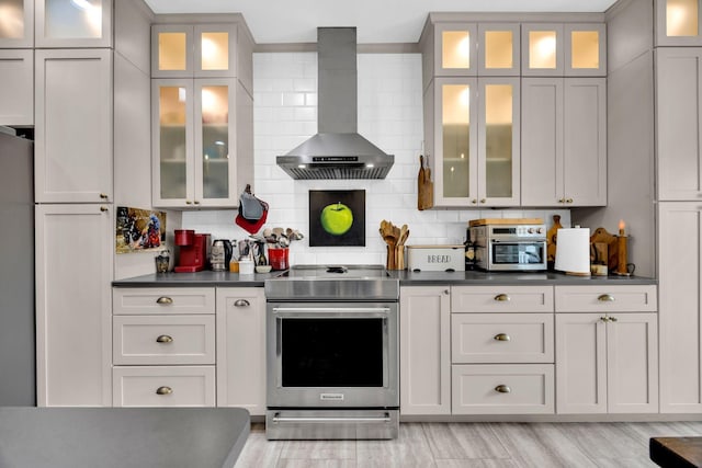 kitchen with wall chimney range hood, backsplash, stainless steel electric stove, dark countertops, and glass insert cabinets