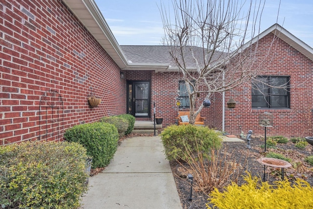 entrance to property featuring a shingled roof and brick siding