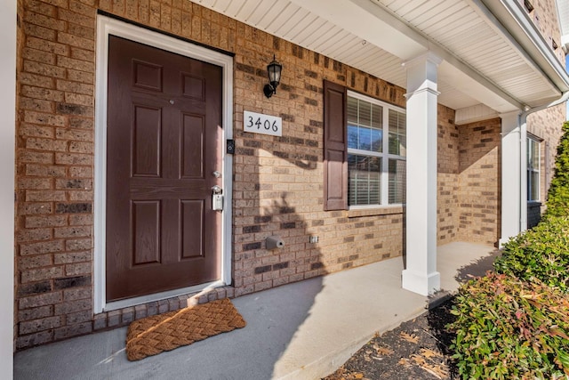 doorway to property with covered porch and brick siding