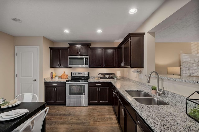 kitchen featuring dark wood-style flooring, stainless steel appliances, a sink, dark brown cabinetry, and light stone countertops