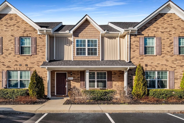 townhome / multi-family property featuring uncovered parking, brick siding, board and batten siding, and roof with shingles