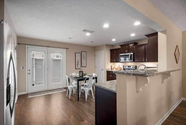 kitchen featuring light stone counters, appliances with stainless steel finishes, dark wood-type flooring, dark brown cabinets, and a kitchen breakfast bar