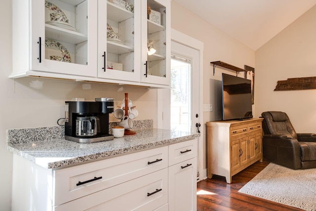 kitchen featuring glass insert cabinets, light stone countertops, vaulted ceiling, dark wood-style floors, and white cabinetry