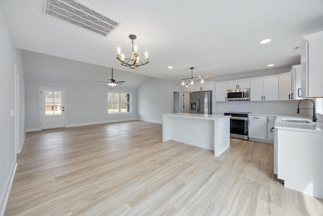 kitchen with visible vents, a kitchen island, appliances with stainless steel finishes, light countertops, and a sink