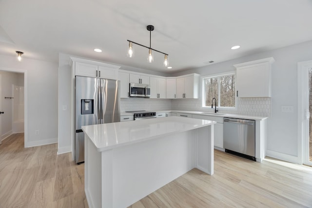 kitchen featuring stainless steel appliances, a center island, white cabinetry, and a sink