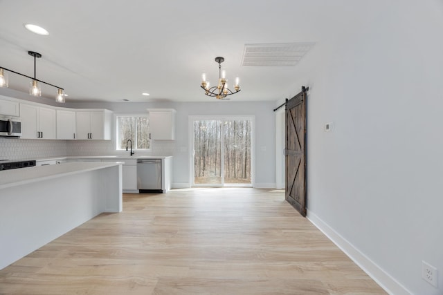 kitchen featuring a barn door, white cabinets, light countertops, appliances with stainless steel finishes, and backsplash