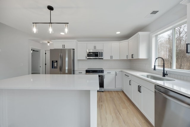 kitchen featuring tasteful backsplash, stainless steel appliances, light countertops, white cabinetry, and a sink