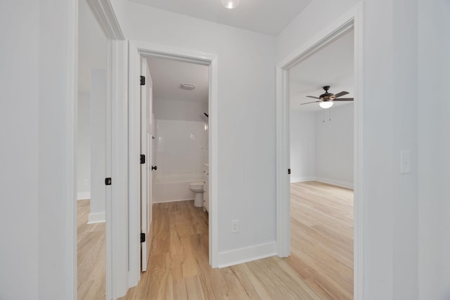 hallway with light wood-style floors, visible vents, and baseboards