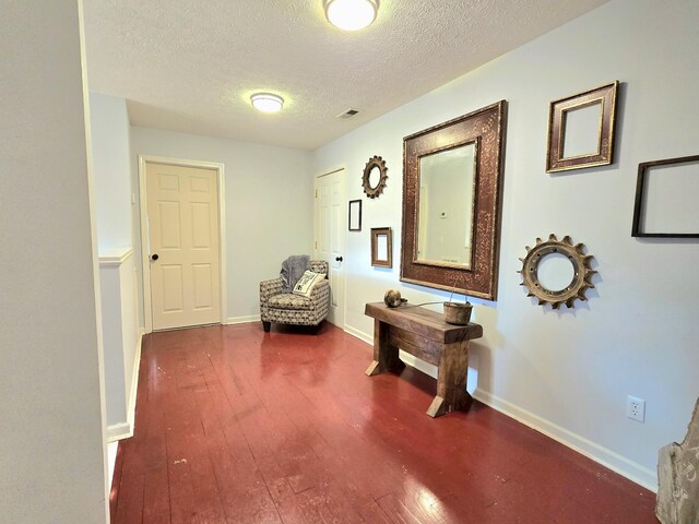 corridor featuring wood-type flooring, visible vents, baseboards, and a textured ceiling