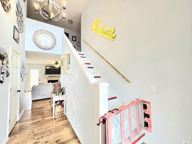 staircase with ceiling fan with notable chandelier, a fireplace, a high ceiling, and wood finished floors