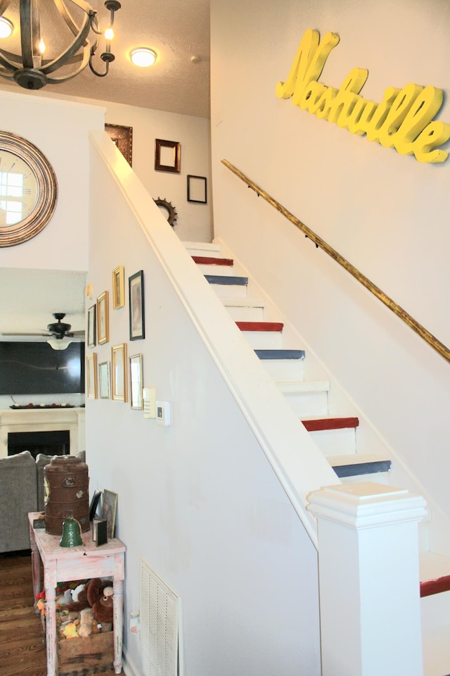 staircase with a textured ceiling, a fireplace, wood finished floors, and visible vents