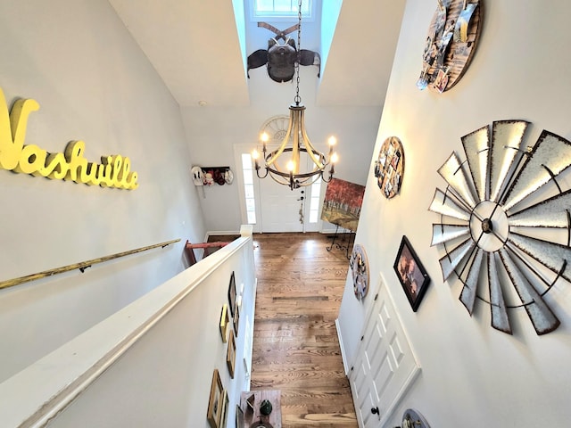 hallway featuring wood finished floors, a towering ceiling, and a notable chandelier