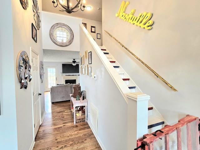 stairs with a fireplace, visible vents, a high ceiling, wood finished floors, and a chandelier