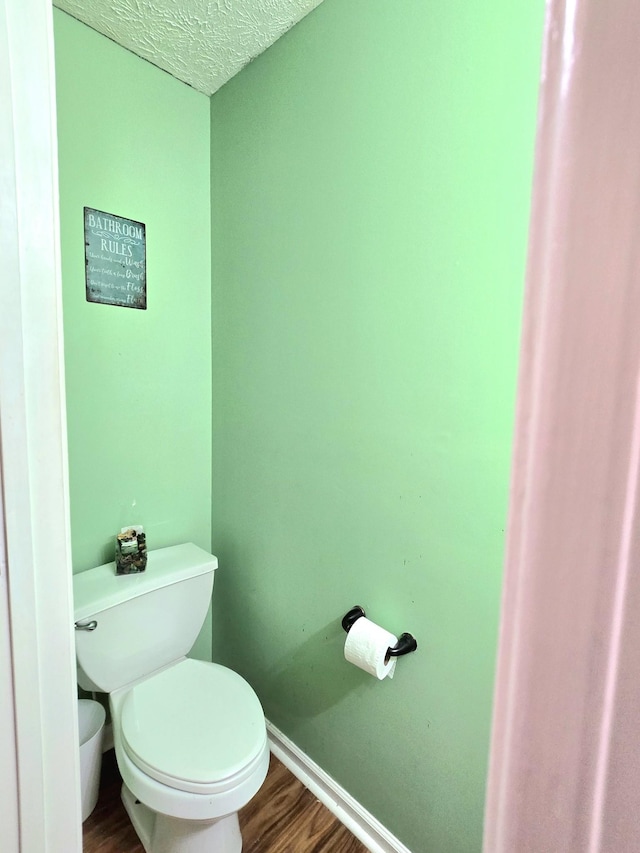 bathroom with toilet, a textured ceiling, baseboards, and wood finished floors