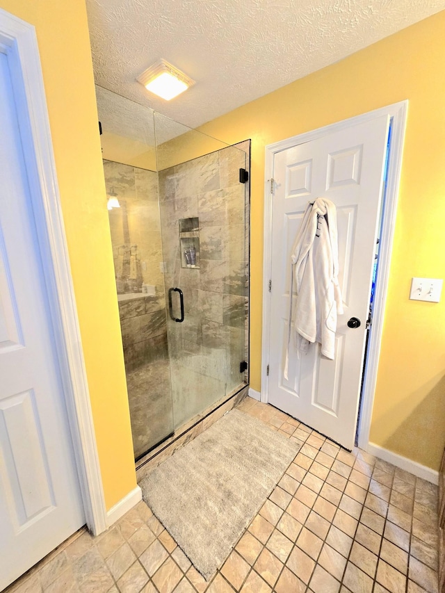 full bath with a stall shower, a textured ceiling, and baseboards