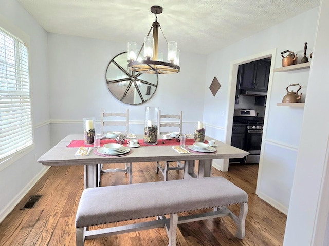 dining area with a textured ceiling, wood finished floors, visible vents, baseboards, and an inviting chandelier