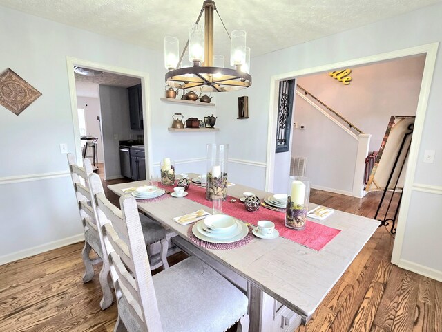 dining area with a notable chandelier, a textured ceiling, and wood finished floors