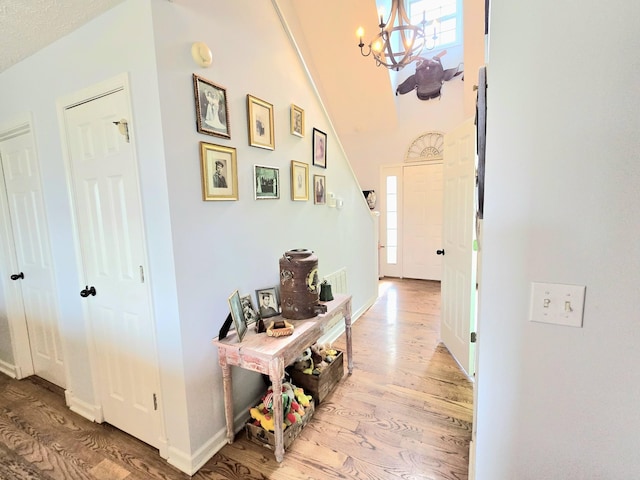 hallway featuring baseboards, wood finished floors, a towering ceiling, and a notable chandelier