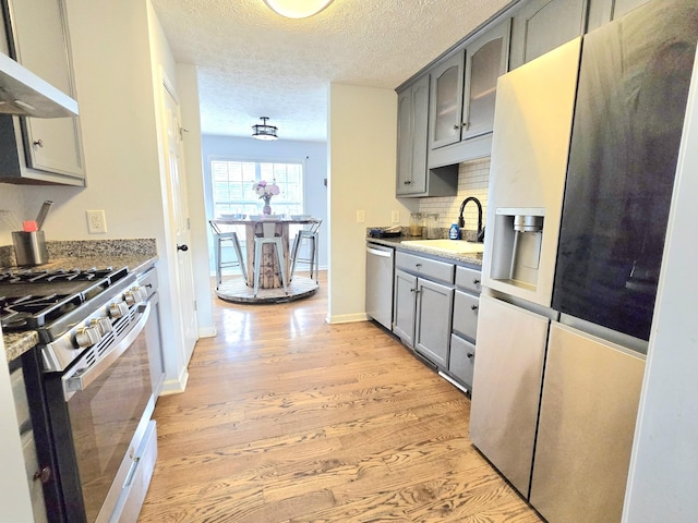 kitchen featuring light wood finished floors, stainless steel appliances, gray cabinetry, under cabinet range hood, and a sink