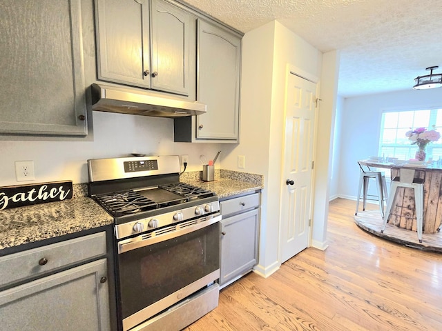 kitchen with light wood-style flooring, gray cabinets, stainless steel gas stove, and under cabinet range hood