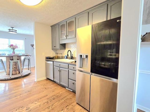 kitchen featuring decorative backsplash, appliances with stainless steel finishes, gray cabinets, light wood-type flooring, and a sink