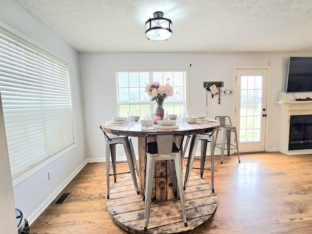 dining space featuring a fireplace, visible vents, a textured ceiling, wood finished floors, and baseboards