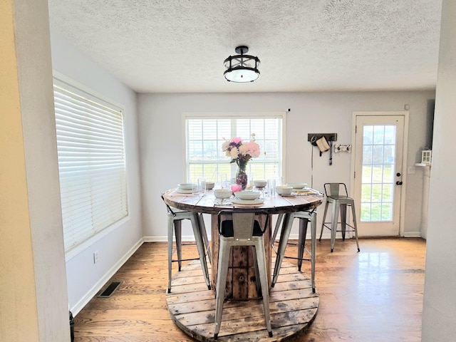 dining area featuring baseboards, a textured ceiling, visible vents, and wood finished floors