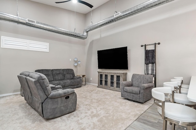 living room featuring ceiling fan, a high ceiling, baseboards, and visible vents