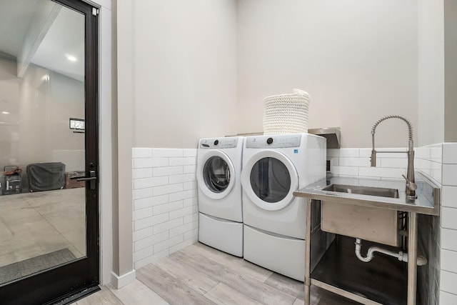 washroom with laundry area, a sink, tile walls, washer and dryer, and light wood-type flooring