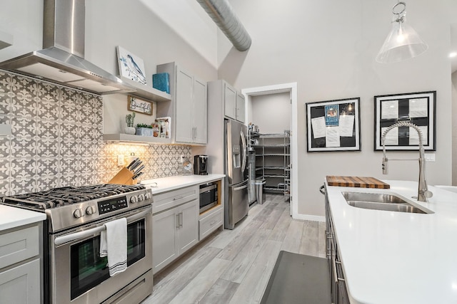 kitchen with decorative backsplash, stainless steel appliances, light countertops, wall chimney range hood, and a sink