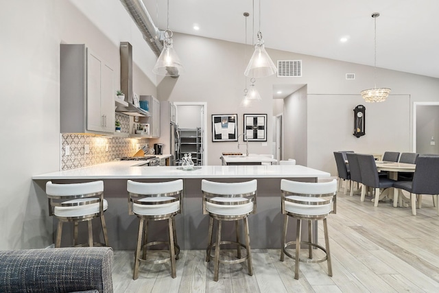 kitchen featuring a peninsula, visible vents, light countertops, light wood-type flooring, and wall chimney exhaust hood