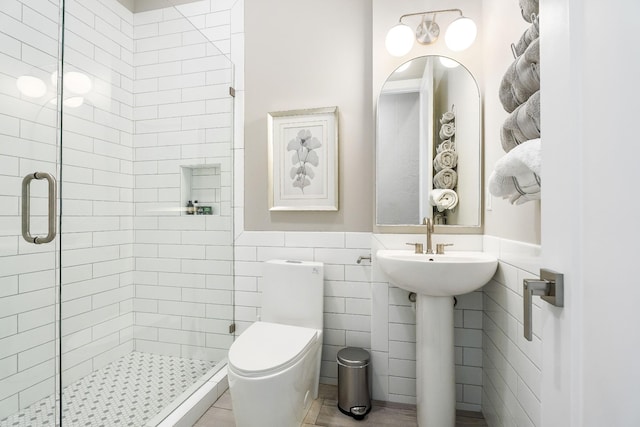 bathroom with tile walls, a wainscoted wall, a shower stall, and toilet