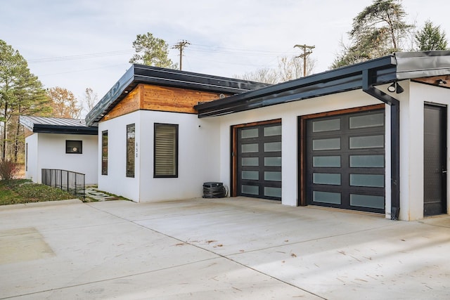 rear view of house featuring a garage, a standing seam roof, metal roof, and concrete driveway