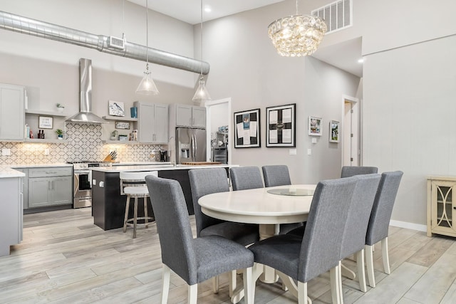 dining area with a chandelier, light wood-type flooring, visible vents, and a high ceiling