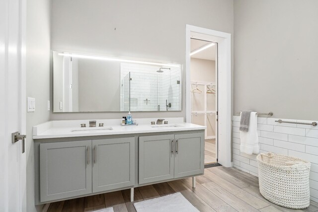 bathroom with a stall shower, double vanity, a sink, and wood finished floors