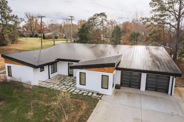 view of front of house featuring metal roof, concrete driveway, stucco siding, a front lawn, and a standing seam roof