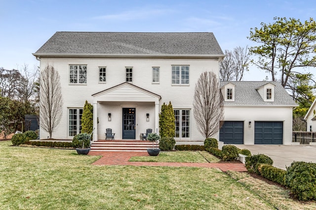 colonial house featuring brick siding, roof with shingles, concrete driveway, an attached garage, and a front lawn